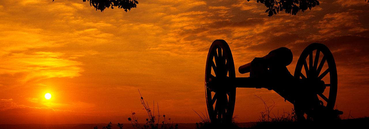 This photo depicts a silhouette of a canon amidst a vibrant, orange sunset. 